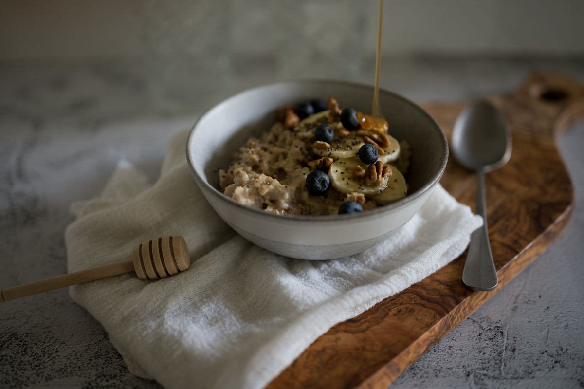 A bowl of hot oatmeal with crushed banana pieces stirred through and a splash of milk being poured in